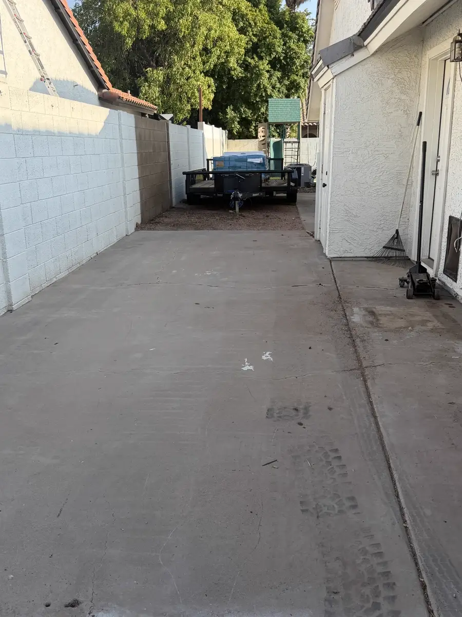 The same side yard after removal: bare swept concrete, with the loaded Roadrunner trailer parked at the far end