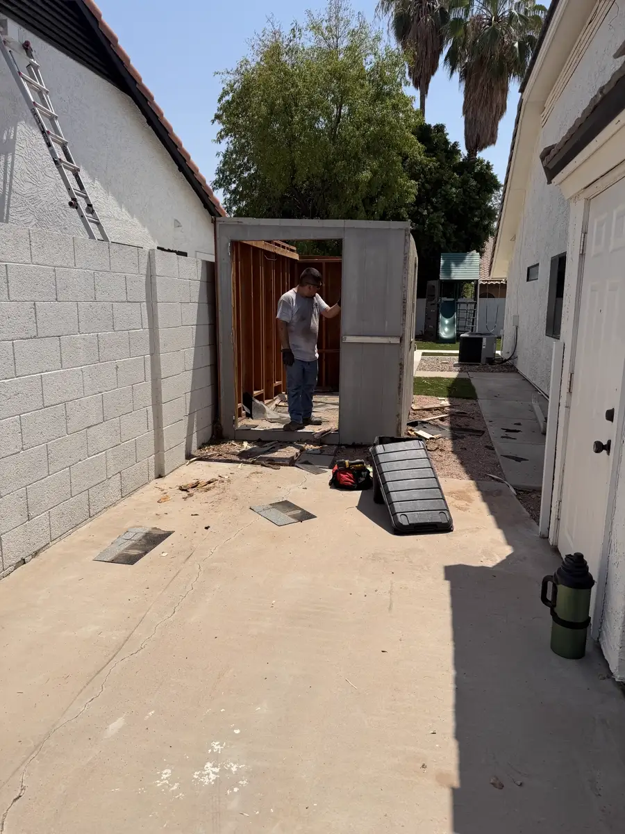 Shed in a narrow side yard being stripped down during removal, tools and debris on the concrete